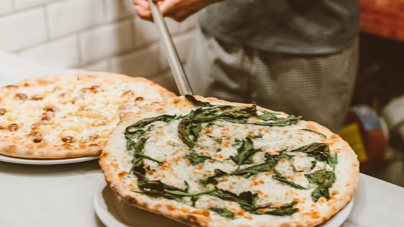 Due pizze appena sfornate sul banco, con la pala del pizzaiolo.